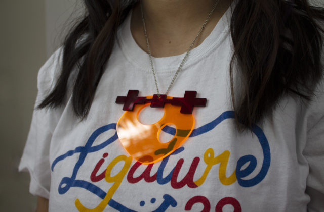 A chunky necklace with an abstract Psyche asteroid and spacecraft hanging on it. The asteroid is neon orange, and the spacecraft is a red.