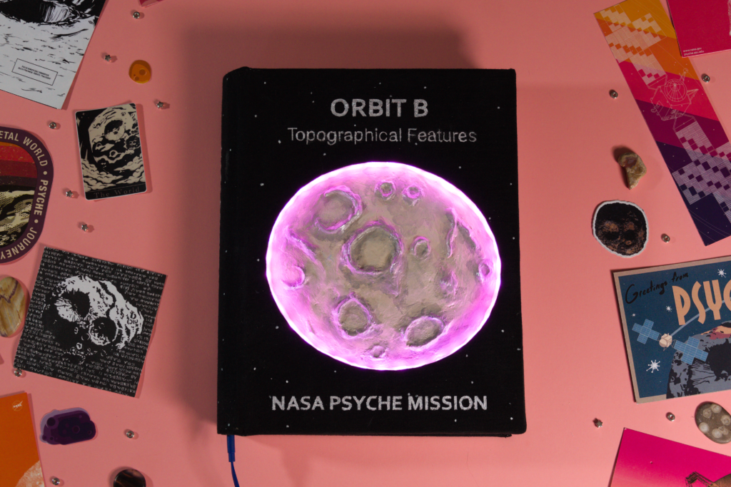 This book is the second in a series about the four orbits the spacecraft will inhabit once it reaches Psyche. The cover features a clay interpretation of the asteroid surrounded by a ring of lights mimicking day and night. The back blurb talks about the mission of orbit B. The interior is hand sewn and finished with marbled end pages.