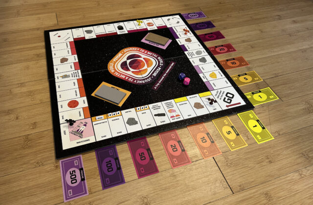 The square board features spaces along the outer edges with asteroids in groups of two or three differentiated by color. The corners of the board are special spaces including “GO,” the launch pad, a gravity assist, and a space that sends you to the launch pad. Accessories including colorful cash, small figurines of the Psyche spacecraft as playing pieces, dice, and two types of action cards.