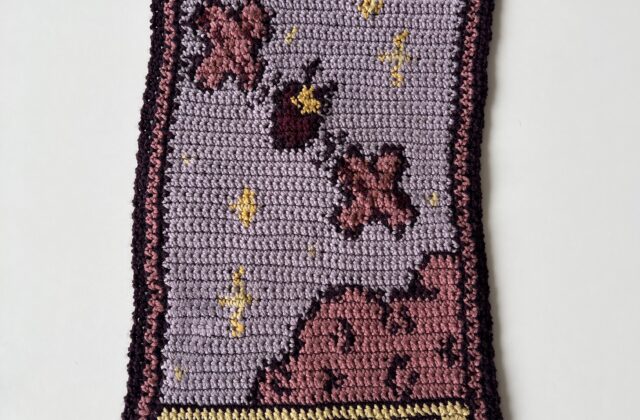 "Tapestry of Psyche" is a crochet tapestry blending medieval artistry with space exploration. Using yarns inspired by the NASA Psyche mission, it features the Psyche spacecraft, stars, and a whimsical cloud. A pixelated "Psyche" graphic adds a modern touch.